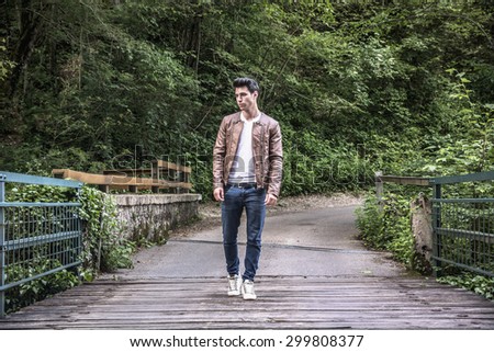 Handsome young man hiking in lush green mountain scenery, crossing a bridge in the forest looking to a side