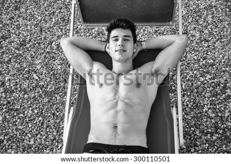 Shirtless Young Man Drying Off in Hot Sun, Muscular Man Wearing Bathing Suit  Sunbathing on Beach Lounge Chair on Beach
