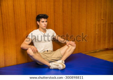 Attractive young man stretching on gym mat, pressing on knees to open legs