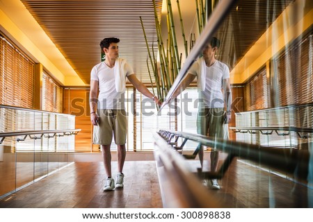 Low Angle View Full Length of Young Man with Towel Over Shoulder Standing in Bright Modern Hallway Holding on to Hand Rail
