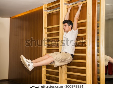 Attractive young man hanging from gym ladder, exercizing abs, looking in front of himself