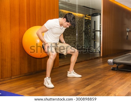 Attractive young man working out with exercize ball against wall to train abs