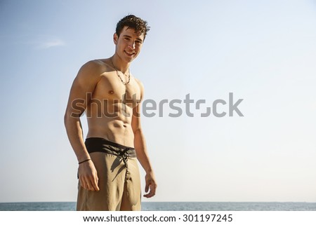 Muscular young man shirtless standing against blue sky, seen from below perspective