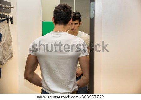 Rear View of a Young Handsome Man Trying on Clothes in Clothing Store\'s Changing Room in Front of a Mirror or in Room Closet