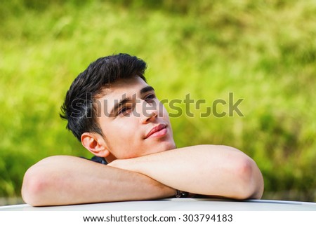 Head and arms shot of handsome attractive young man looking at camera outdoor, leaning on flat surface with head resting on hands