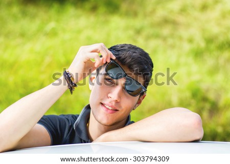 Head and arms shot of handsome attractive young man looking at camera outdoor, leaning on flat surface with head resting on hands