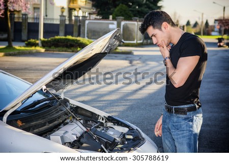 Handsome young man trying to repair a car engine, looking inside open bonnet
