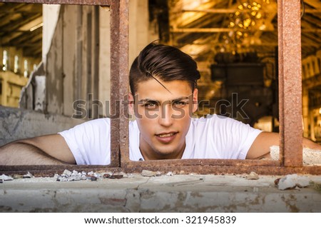 Attractive young man at rusty window with happy expression on his face, looking in camera
