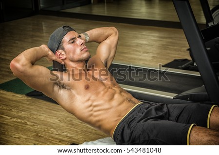 Attractive muscular young man shirtless in gym working out, doing exercises for abs