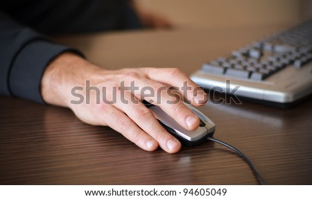 Hand of a man working at computer clicking on mouse on dark desktop