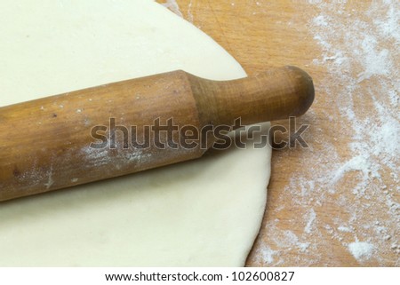 Rolled out dough and rolling pin lying on a wooden board sprinkled with flour