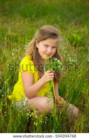 Sweet blonde little girl smelling field flowers on the meadow