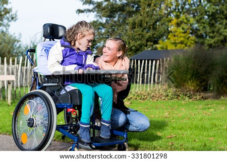 Disability a disabled child in wheelchair relaxing outside with a care assistant/ Disability a disabled child in wheelchair relaxing outside