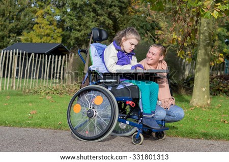 Disability a disabled child in wheelchair relaxing outside together  with a care assistant/ Disability a disabled child in wheelchair relaxing outside