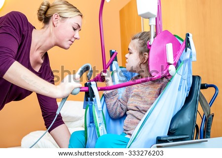 A disabled child being lifted into a wheelchair by a care assistant/ Disabled child