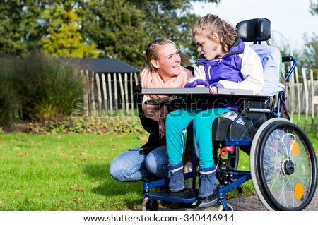 Disability a disabled child in a wheelchair relaxing outside with a care assistant / Disability a disabled child in a wheelchair relaxing outside