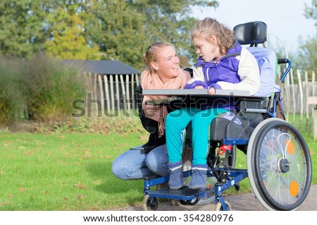 Disability a disabled child in a wheelchair relaxing outside together with a carer / Disability a disabled child in a wheelchair relaxing outside