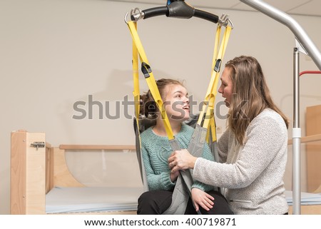 Disabled person being lifted into a wheelchair using special needs equipment together with a nurse / Working with disability