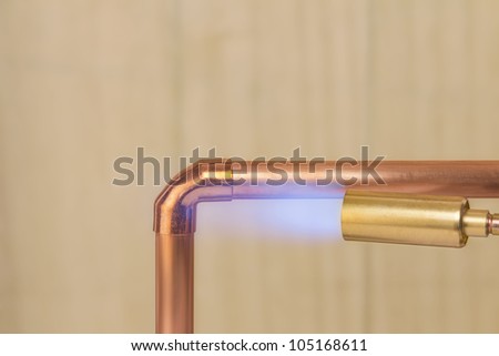 A plumbers hot gas soldering burner heating a copper elbow fitting to join two copper water pipes