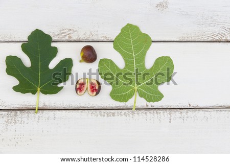 Ripe fresh fig fruits and leaves on white rustic wooden board with copyspace