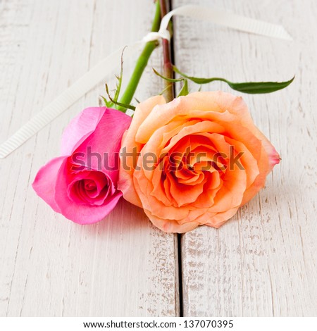 Two beautiful orange and pink roses on tight together on rustic wood table.