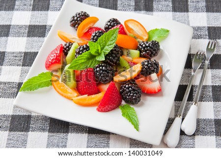 Fruit salad with fresh strawberries, blackberries,  kiwis and  kumquats on white plate. Healthy eating, berry dessert. selective focus.
