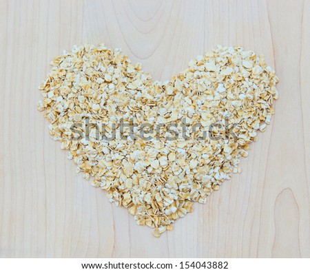 Whole grain oats in heart shape on wooden board, healthy food.