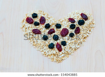 Whole grain oats with dried cranberries and blueberries in heart shape on wooden board, healthy food.