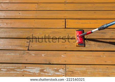 Wood stain with a paint pad  on wooden deck floor.