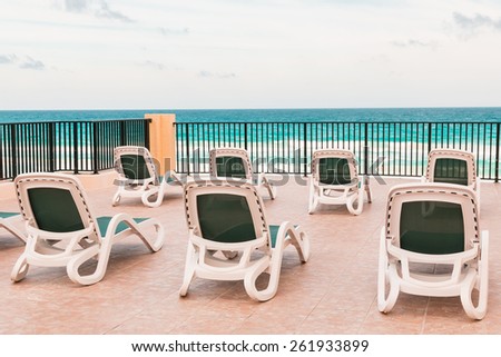 Empty lounge chairs for sunbathing on patio near ocean beach.