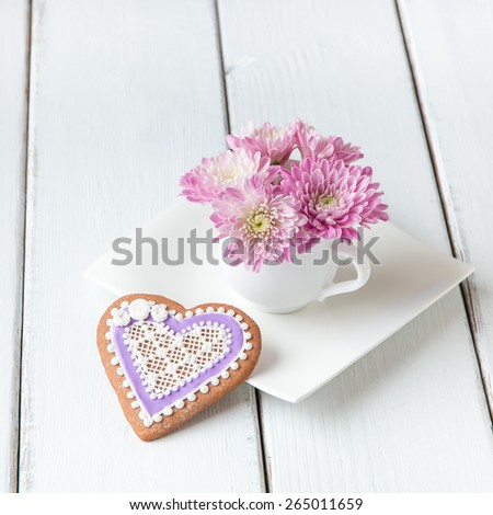 Cup full of pink  mum flowers and  heart shape cookie on white wooden table.