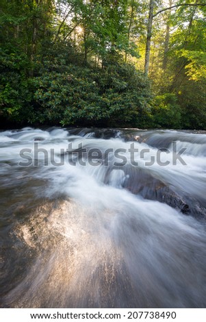 The sun starting to peak out in the early morning along a brisk moving cascade on South Mills river in the Blue Ridge Mountains of North Carolina.