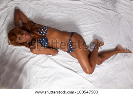 Lovely African American woman laying down on her back in a blue with white dots, two piece swimsuit, her  skin glistening, her knees bent, viewed from above