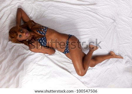 Lovely African American woman laying down on her back in a blue with white dots, two piece swimsuit, her  skin glistening, her knees bent, viewed from above