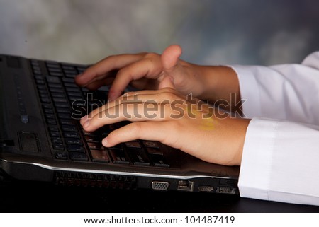 Hands typing on a laptop keyboard while wearing a white lab coat