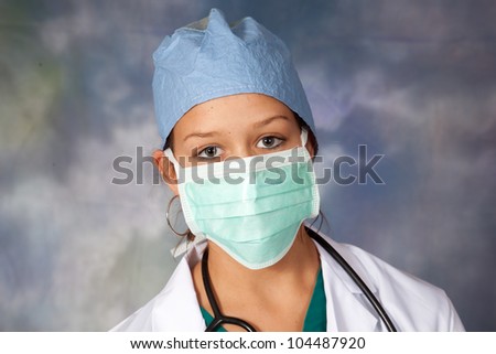 Female medical person in white lab coat, surgery hat and surgery mask around her face, looking at the camera
