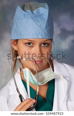 Female medical person in white lab coat, surgery hat and surgery mask around her neck, and a stethoscope draped across her shoulders, smiling at the camera