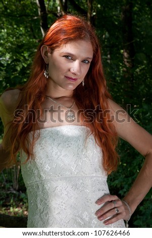 Pretty redhead bride in her wedding dress,  outside  looking at the camera with a thoughtful expression