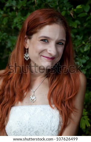 Pretty redhead bride in her wedding dress, looking at the camera with a thoughtful expression and a playful smile