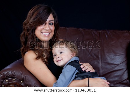 Mother holding her son on her lap and hugging him with both smile broadly with affection