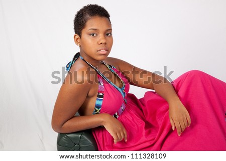 Pretty black woman in red dress relaxing and leaning back on a couch, looking at the camera with a serious but friendly expression