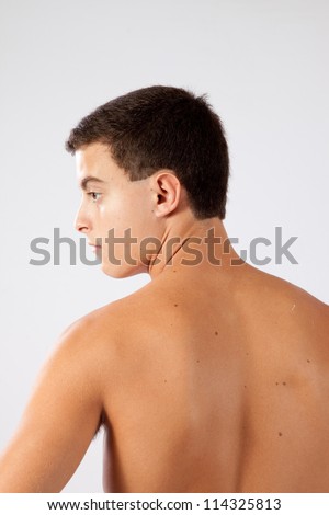 Young athletic teenage boy with his shirt off,  with his back to the camera and looking to the left
