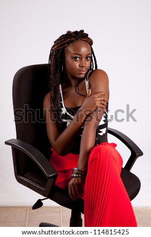 Lovely black woman in red slacks sitting in a black business chair and holding her arm