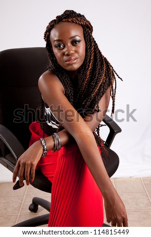 Lovely black woman in red slacks sitting in a black business chair and crossing her arms on her lap