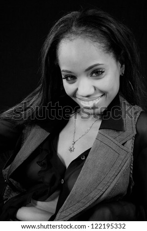 Lovely black woman in a black shirt and a vest, sitting with a friendly and serious expression of flirting with the camera in black and white