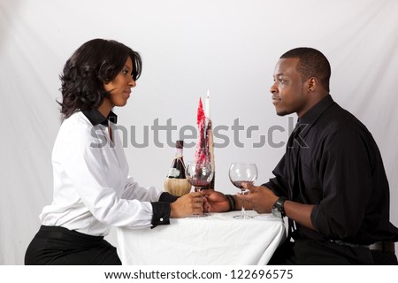 Romantic black couple sitting face to face at a table with a candle, a bottle of wine and two wine glasses for a dating view