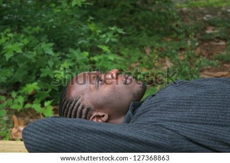 Handsome African American man laying down outside on a wooden dock with his hands behind his head and looking up at the sky