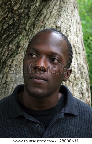 Handsome African American man outside looking left and standing beside a rough tree