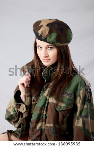 Pretty woman in a military camouflage jacket and beret hat, looking at the camera with a friendly, sexy smile and holding the lapel of her jacket