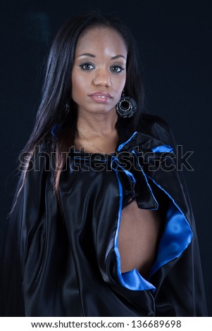 Beautiful black woman wearing a cape that is black on the outside and blue on the inside, with no blouse on underneath the cape, displaying a bit of her abdomen